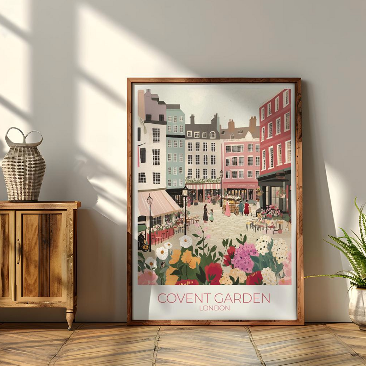 Framed illustration of Covent Garden, London, showing a vibrant market scene with colorful buildings, flower stalls, and people. The print hangs above a wooden dining table set with kitchenware, with white subway tiles and shelves in the background. Text on the print reads 'COVENT GARDEN LONDON'.