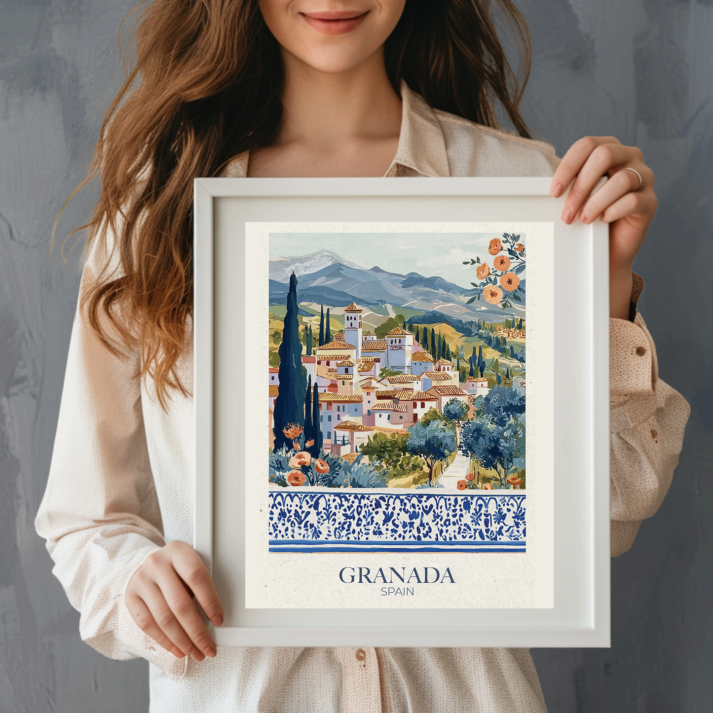 Woman holding a framed artwork of Granada, Spain with mountains and buildings.