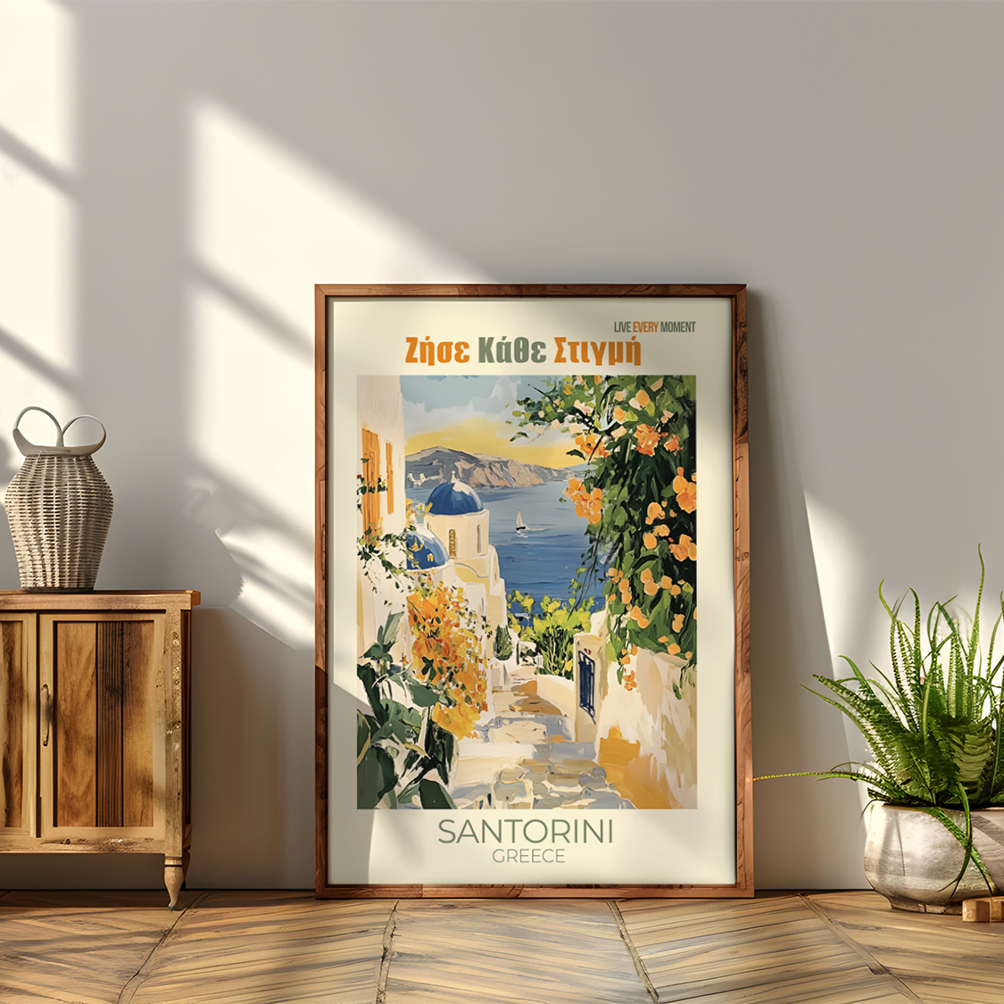Framed poster of Santorini with a wooden cabinet and plants in a room.