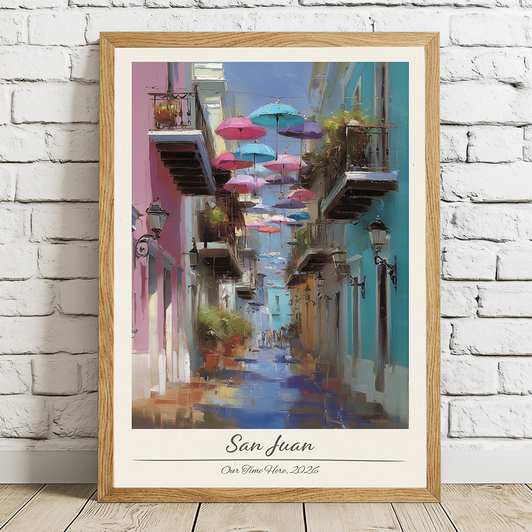 Framed artwork of a colorful street scene with umbrellas in San Juan, displayed on a white brick wall.