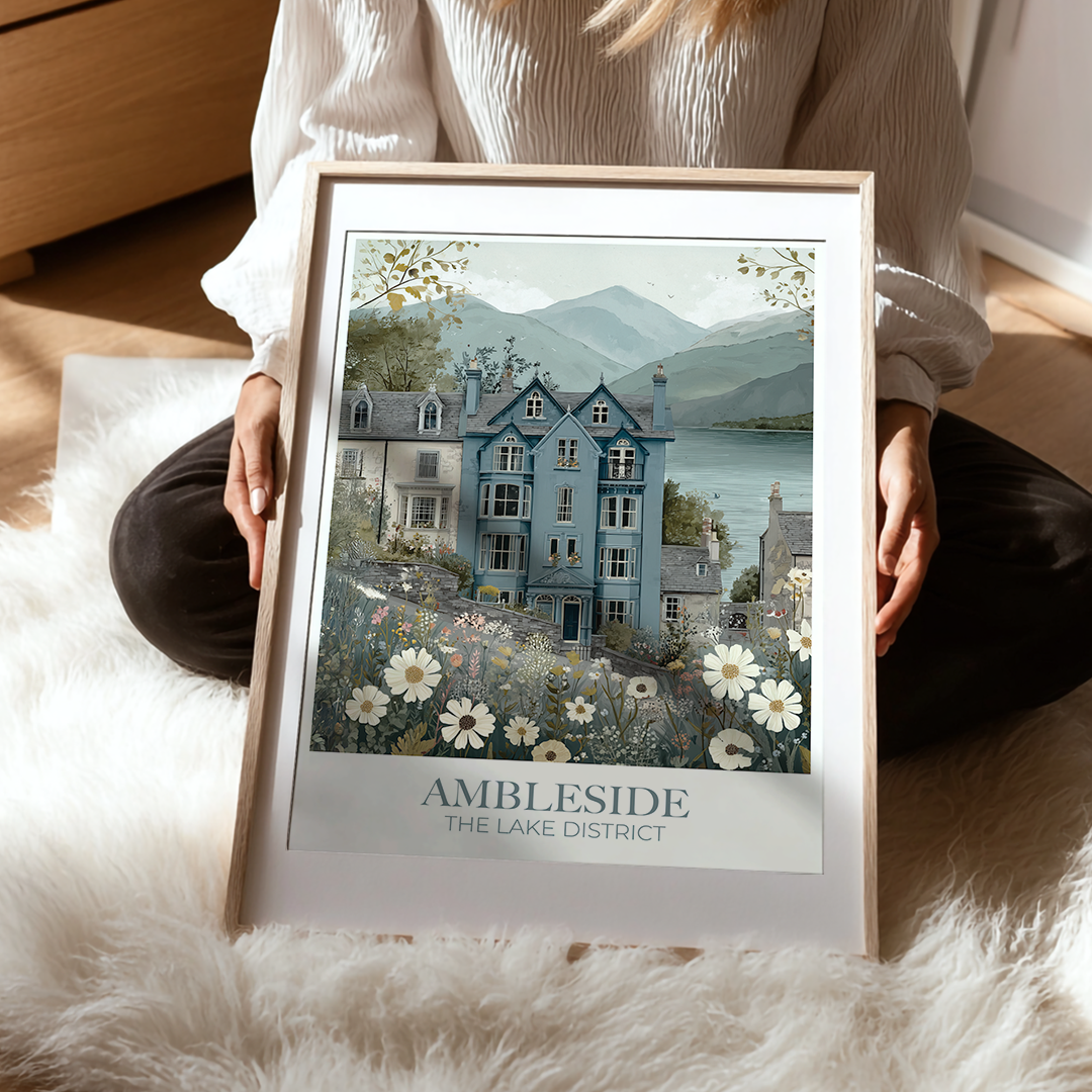 Person holding a framed print of a scenic house with 'Ambleside' text on a soft surface.