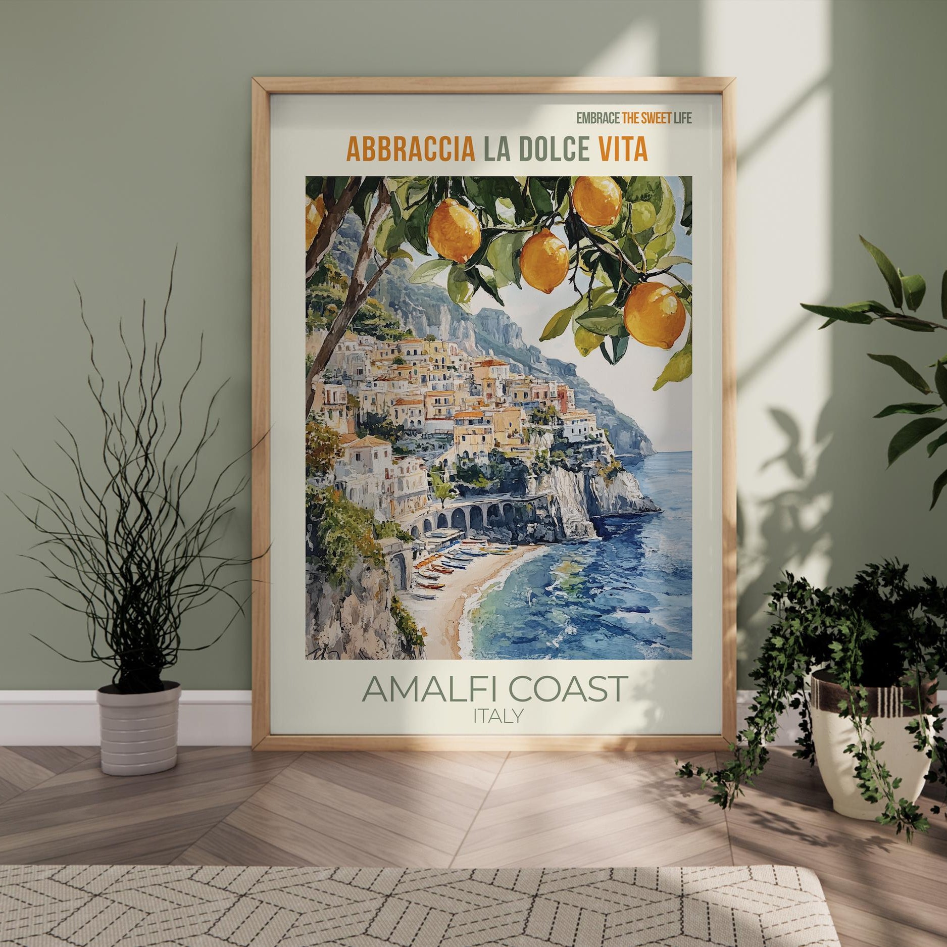 Framed poster of the Amalfi Coast with oranges on a wall in a room with plants.