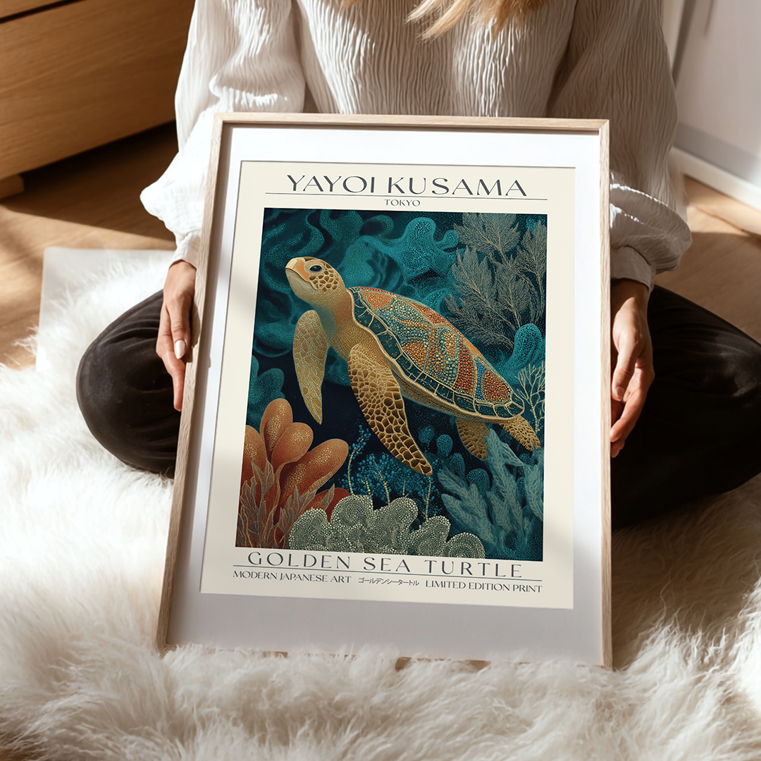 Framed artwork of a sea turtle by Yayoi Kusama held by a person on a soft surface.