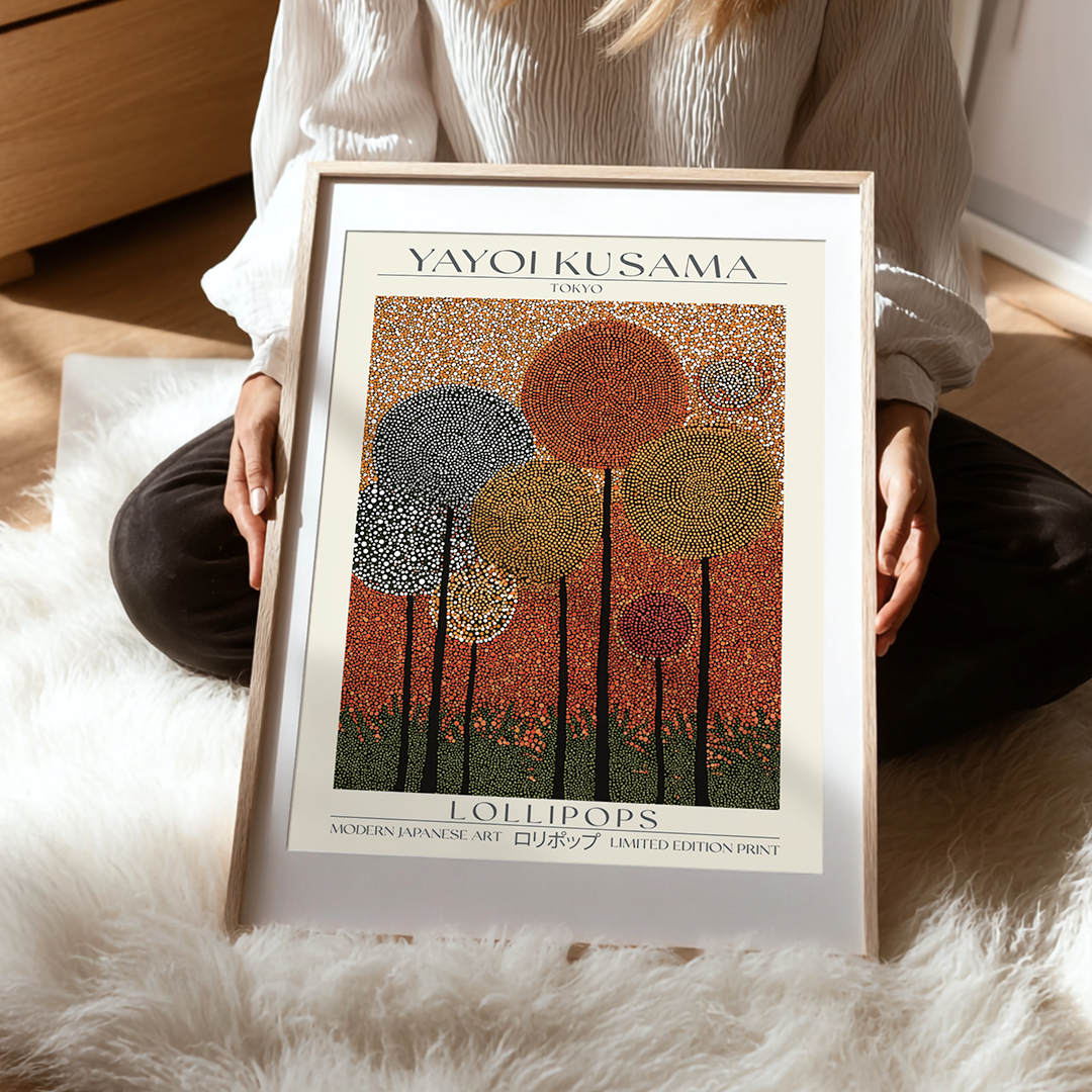Person holding a framed Yayoi Kusama art print titled 'Lollipops' on a soft surface.