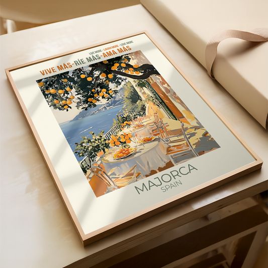 Framed artwork of a scenic table setting with oranges, labeled 'Majorca Spain', on a light wooden surface.