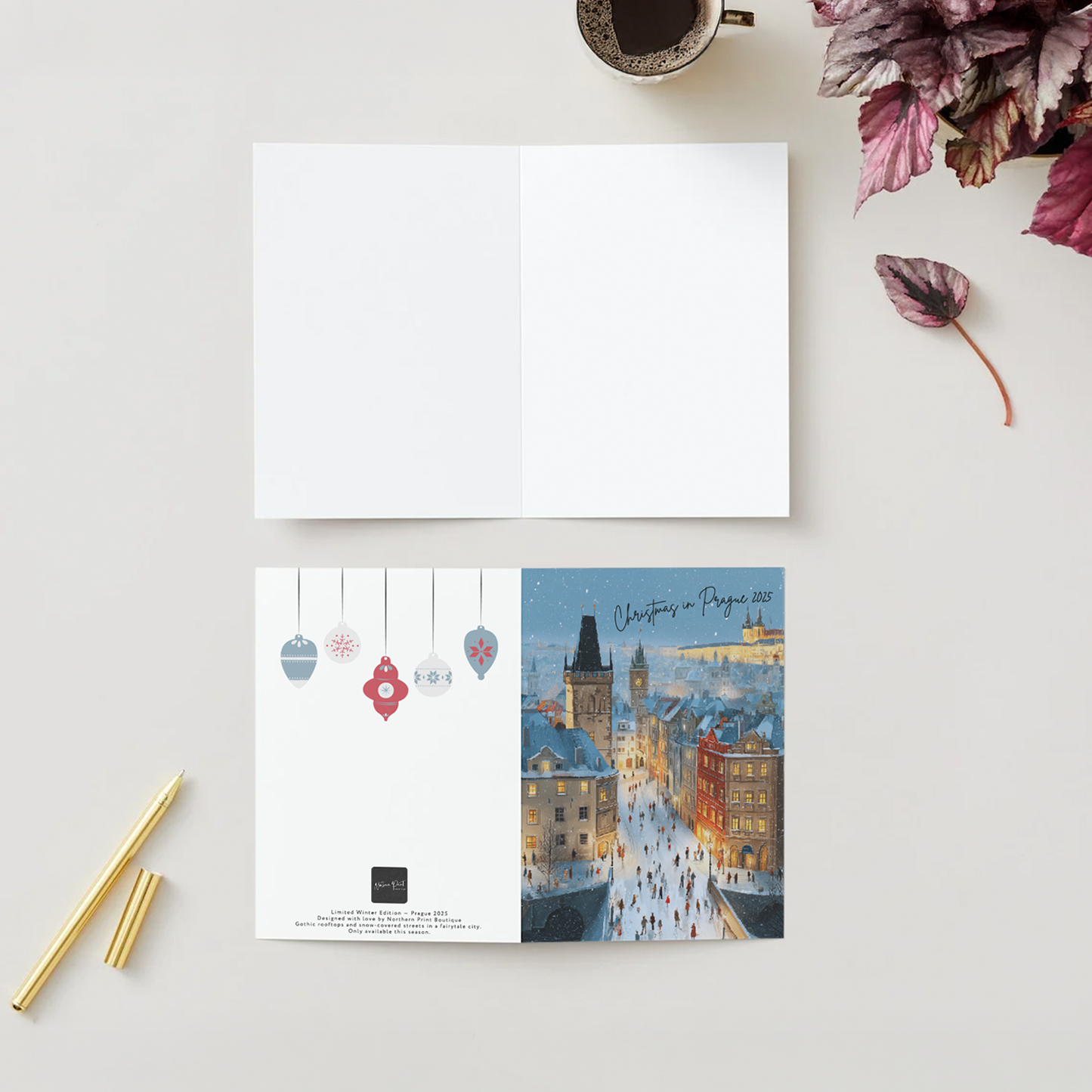 Open book with Christmas-themed illustration of Prague on a white surface with a cup of coffee and flowers.