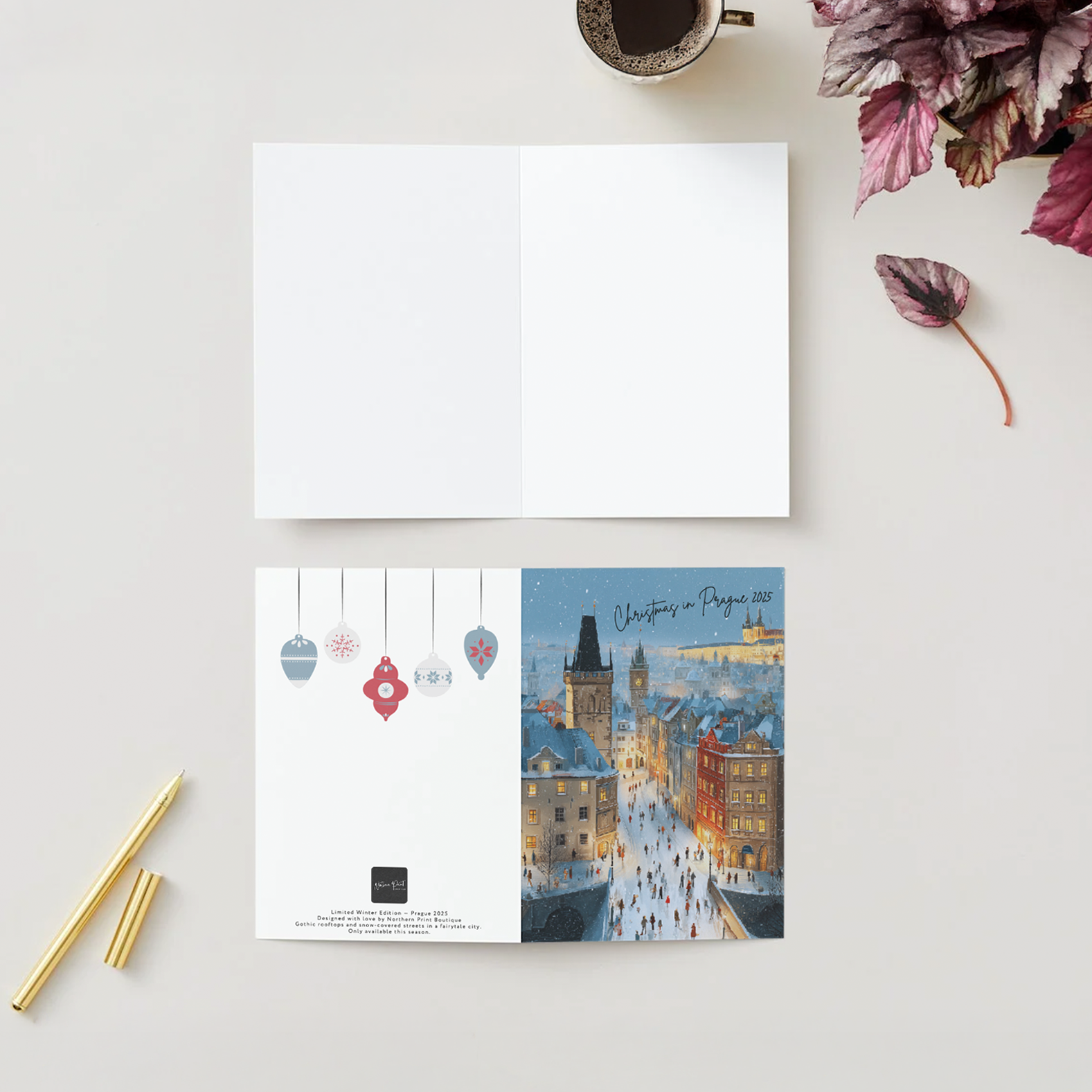 Open book with Christmas-themed illustration of Prague on a white surface with a cup of coffee and flowers.