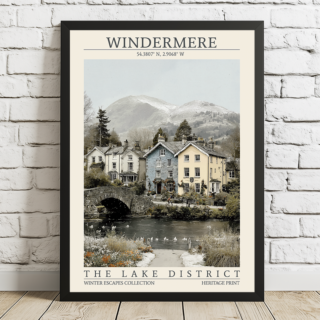 Framed print of a scenic view of houses by a lake with mountains in the background, displayed on a white brick wall.